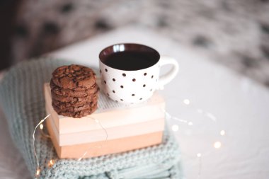 Bir fincan siyah çay ve çikolatalı kurabiyeler kitap yığınının üzerinde duruyor ve yatakta örülmüş süveter. İyi sabahlar. Kahvaltıda. Gece vakti.. 