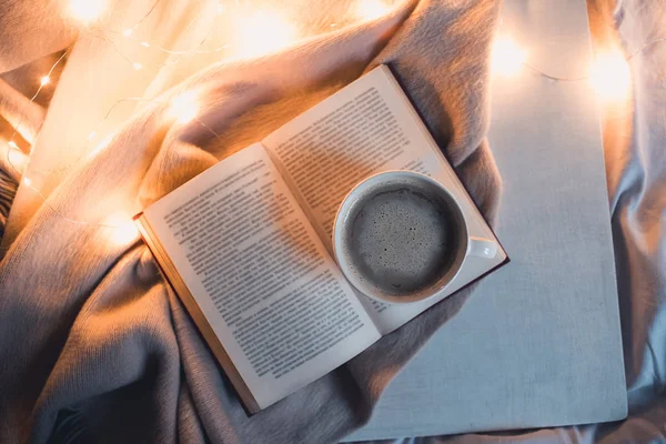 Geceleri yatakta bir fincan kahveyle açık bir kitap. Üst görünüm. 