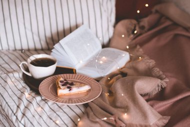 Lezzetli meyveli turta, taze siyah çay ve parlak ışıkları olan ahşap tepside açık kitap. İyi sabahlar. Kahvaltı zamanı.. 