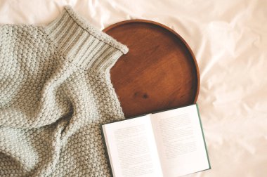 İyi sabahlar. Açık bir kitap ve ahşap tepsiyle örülmüş bir kazak. Sonbahar mevsimi. 