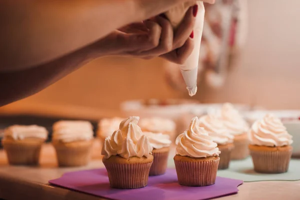 Mutfak masasının üzerinde krem peynirle kapkek süsleyen kadın. Doğum günü partisine hazırlanıyorum.. 
