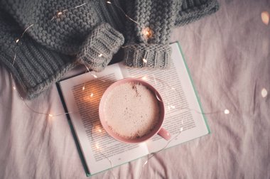 Yatakta kahve molası. Bir fincan latte, örgü süveterle açık bir kitap gibi duruyor. İyi sabahlar. Kış mevsimi. 