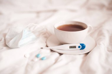 Bir fincan taze çay ve termometre, yüksek ısıtıcı, ilaç ve tıbbi maske. Hastalık konsepti. Sosyal izolasyon.  