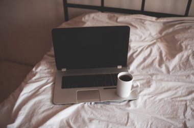 Yatakta bir fincan kahveyle bilgisayarda çalışıyor. Odada yakın plan. Karantina zamanı. Evde kal. İyi sabahlar. Kahvaltı.. 