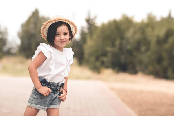 笑顔の子供の女の子4 5歳は屋外公園でわら帽子 白い上とデニムのショートパンツを着ています カメラを見て 夏のシーズン 休暇の時間 — ストック写真