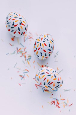 Paskalya yumurtası. Minimalist el boyaması. Yumurta fotoğrafı. Yumurtalarda renkli taç yaprakları. Parlak ruh hali. Duygular. Kırmızı elementler Fırçala ve boya çiz. Renk desenleri. Beyaz arka planda yumurtalar ve dağınık şekerleme serpintileri. Parlak yemek. Lezzetli yumurtalar.