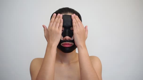 白い背景の上に彼女の顔にマスクを浄化と顔面のブラック マスク シートを行う若い女性 — ストック動画