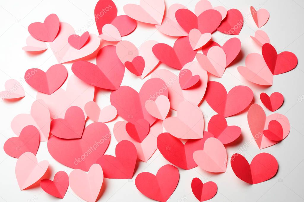 Bunch of cut out of pink and red paper hearts on white background.