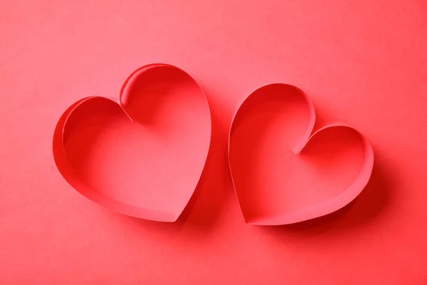 Pair of red paper hearts on red background top view