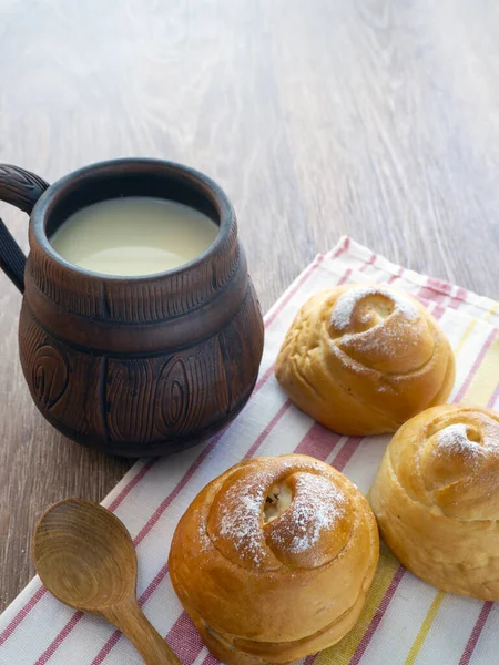 Delicious sweet buns with milk for breakfast. Milk is poured into a clay mug. Rustic food