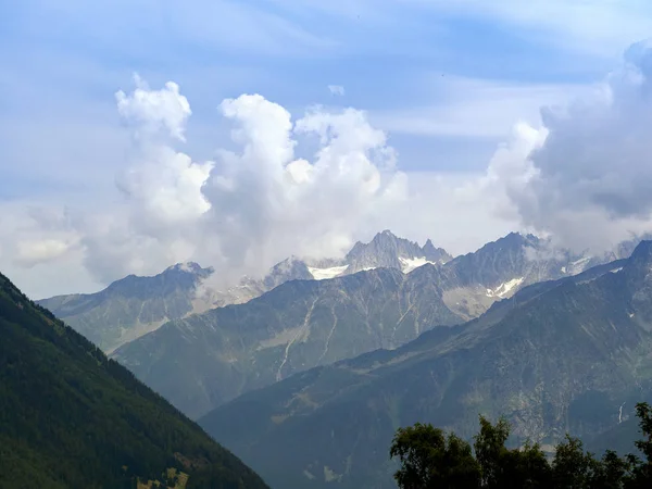 Pegunungan di Pegunungan Alpen sejajar satu sama lain. Awan yang indah terletak di puncak gunung. Hutan konifer tumbuh di lereng terdekat . — Stok Foto