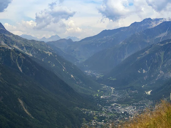 A cidade está localizada no vale dos Alpes. Altas montanhas erguem-se. As encostas das montanhas são verdes . — Fotografia de Stock