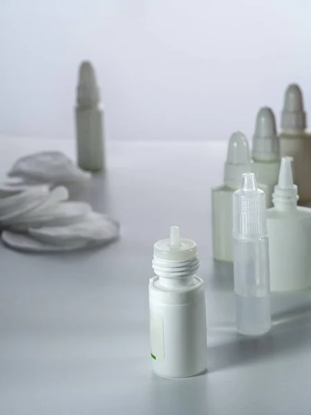 Droppers and sprays with different medicines for the eyes and nose, as well as cotton pads, are on a vertical background.