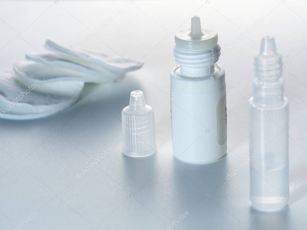 Cotton pads and preparations for eye or nasal diseases in droppers are located on a simple horizontal background.