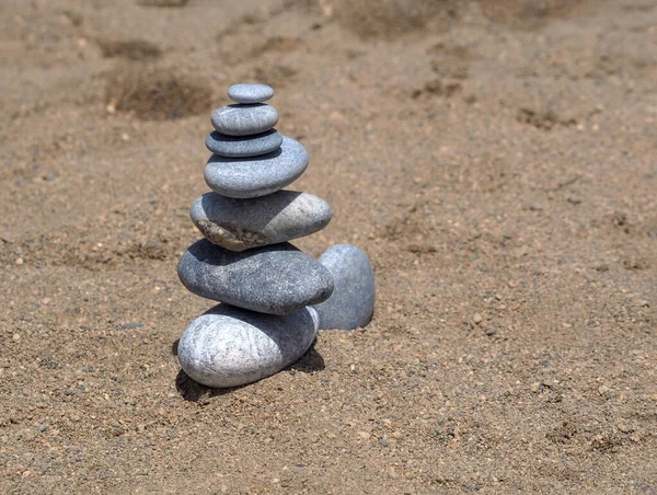 平らな石と丸い石で作られた細かい砂の上に石のピラミッド。夏の穏やかな背景. — ストック写真