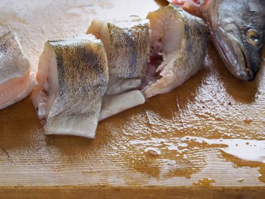 Parçalara ayrılmış taze bir balık kesme tahtasının üzerinde yatıyor. Balık yemekleri pişiriyorum..