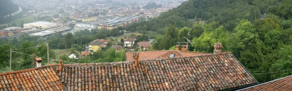 房子的屋顶上铺着粘土瓦 在山谷的屋顶后面 可以看到有人居住的地方和树木 横向全景 有瓦片屋顶和城市的背景 — 图库照片