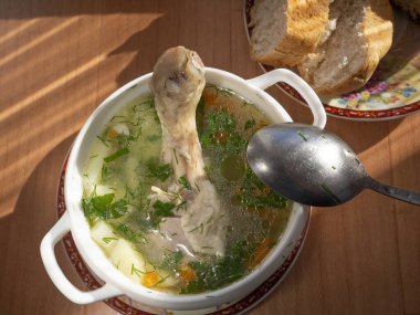 Öğle yemeğinde iştah açıcı tavuk çorbası. Tavuk çorbasının yüzeyinde sebzeler ve yağ damlacıkları görülebilir. Masanın üzerinde bir tabak ekmek var..