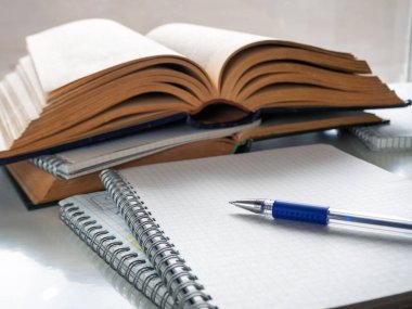 Kalem boş bir defter kağıdının üzerinde yatıyor. Yakınlarda açık kitaplar ve defterler var. Okuma, bilimsel çalışma, soyut çalışma, edebiyat eğitimi. Kitap, defter ve kalemle arka plan.