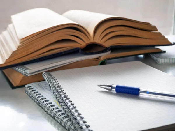 Kalem boş bir defter kağıdının üzerinde yatıyor. Yakınlarda açık kitaplar ve defterler var. Okuma, bilimsel çalışma, soyut çalışma, edebiyat eğitimi. Kitap, defter ve kalemle arka plan.