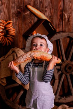 Şef önlüğü ve şapka yiyen küçük bir çocuk. Masa dağınık. Havası çok güzel. Etrafta bir sürü malzeme ve farklı şeyler var. Fırın için kavram.