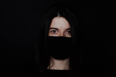 Siyah arka planda koruyucu maskeli genç bir kız. Siyah saçlı ve kırmızı maskeli bir kız. Koronavirüs hastalığına karşı. Salgın Coronovirus covid-19 salgını. Ev konseptinde kal.