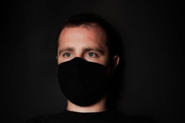 Siyah arka planda koruyucu maskeli genç bir adam. Siyah saçlı ve siyah maskeli bir adam. Koronavirüs hastalığına karşı. Salgın Coronovirus covid-19 salgını. Ev konseptinde kal.