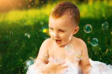 Köydeki mutlu çocuk büyük bir kase köpük ve kabarcığın içinde banyo yapıyor. Mutlu tasasız çocukluk. Yazın kırsal kesimde. Bir sürü köpük ve köpük. Güzel yeşil çimenler. Güneş parlıyor.