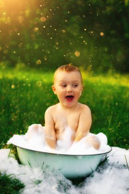 Köydeki mutlu çocuk büyük bir kase köpük ve kabarcığın içinde banyo yapıyor. Mutlu tasasız çocukluk. Yazın kırsal kesimde. Bir sürü köpük ve köpük. Güzel yeşil çimenler. Güneş parlıyor.