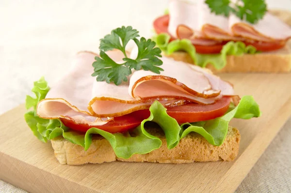 Vista ravvicinata di pane tostato, lattuga, pomodoro, salumi sul tagliere — Foto Stock