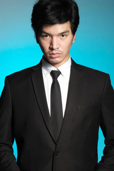 Asian man in black suit and white shirt on blue background — Stock Photo, Image