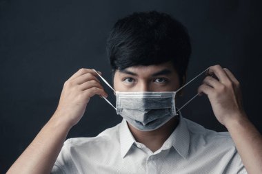 Yüzünde siyah arka planda tıbbi maskesi olan Asyalı bir adam.