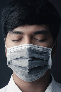 Yüzünde siyah arka planda tıbbi maskesi olan Asyalı bir adam.