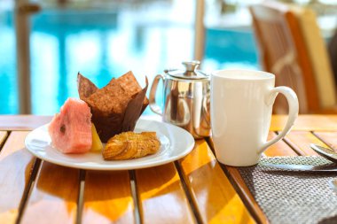 Kahvaltı, kapuçino ve bir tabak kruvasan, kek ve taze meyve.