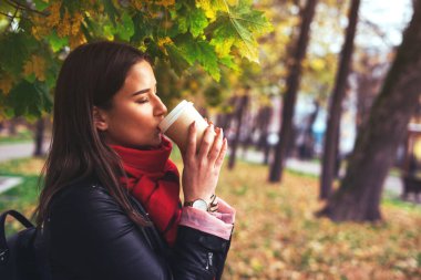 Kız sonbahar parkında sıcak bir içki içiyor..