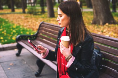 İçki ve telefonla bankta oturan bir kadın..