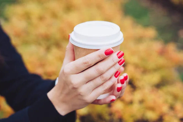 Hot drink in the hands of a girl with red manicure close up.
