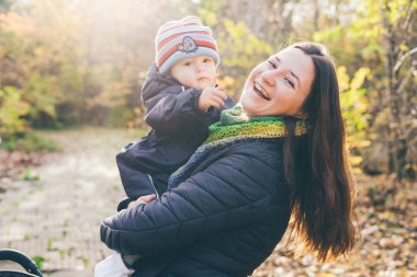 Anne oğluyla birlikte güneş ışığında sonbahar bahçesinde duruyor..