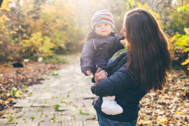 Anne oğluyla birlikte güneş ışığında sonbahar bahçesinde duruyor..