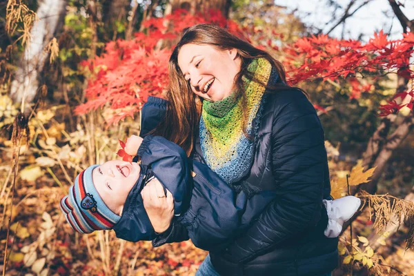 Madre con un bebé en brazos en un jardín botánico jugando entre sí . — Foto de Stock