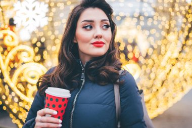 Makyajlı bir kadın Noel ışıklarının arka planına yan bakıyor.