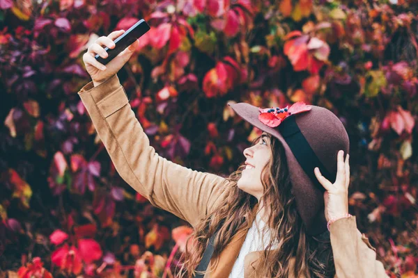 Frau mit Hut macht Selfie auf dem Hintergrund von Herbstblättern. — Stockfoto