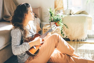 Genç ve güzel bir kadın ukulele çalar, güneşte şarkı söyler..