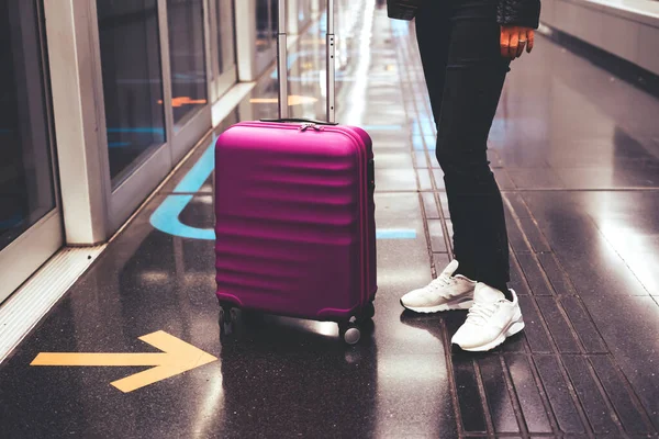 Violetter Koffer steht neben einer Frau, die in Flughafen-U-Bahn steht. — Stockfoto