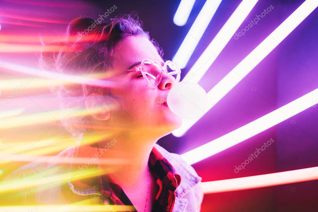 Millennial girl blowing bubble gum illuminated neon light.