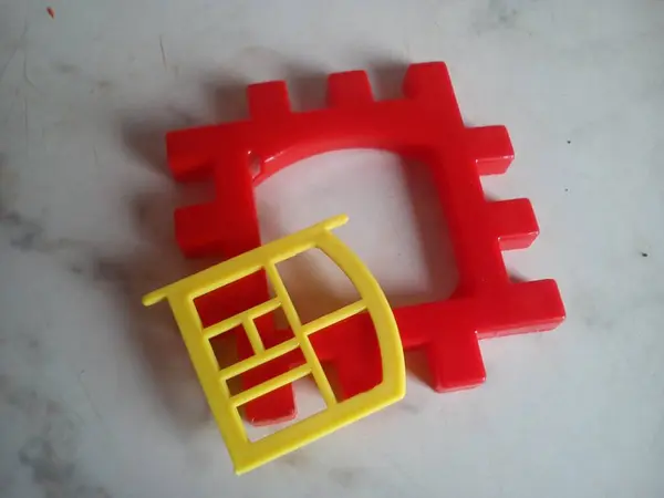 Panel de plástico de juguete para casas prefabricadas con ventana rota. Detalle rojo con marco de ventana amarillo. El juguete está sobre un fondo claro . — Foto de Stock