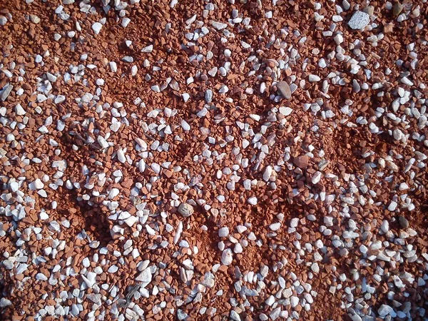 Fine decorative color granite crushed stone. Red-brown colored stone chips are used for landscaping. Crushed marble, granite, gravel or sand. Spots of fine white pebbles on heterogeneous soil