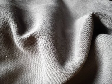 Yakın çekim ve gri örgü kumaş dokusu, hafif kıvrımlı ya da buruşuk. Gün ışığında makine örgü kumaşında ışık ve gölge oyunu. Yumuşak, kalın, sıcak pamuklu kumaş.