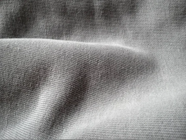 Texture of a gray knitted fabric, slightly folded in waves or wrinkled. The play of light and shadow on a machine-knitted fabric in natural daylight. Soft, thick cotton material — Stock Photo, Image