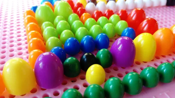子供のモザイクからピンクのプラスチックパネル。明るい教育のおもちゃ。青、赤、ピンク、黄色、緑、紫の固体プラスチックボール。カラフルなモザイクの詳細は丸い穴に立ち往生している. — ストック写真